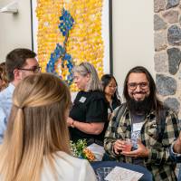 Group of event attendees standing around table, chatting with each other and laughing